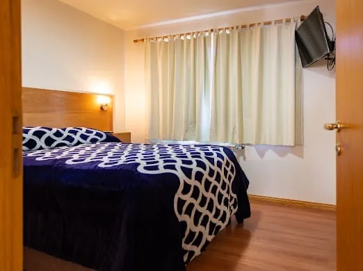 Living con hogar a leña, techo de madera y sillón floral en cabaña de Villa Los Coihues, Bariloche